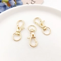 Close-up of three gold zinc alloy lobster clasps with swivel D-rings on a ceramic plate - KC Gold