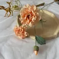 Detail of faux champagne peony silk flowers with realistic petals and green buds on a table - Orange
