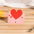 Pink greeting card with red 3D heart cutout and love quote on a wooden desk surface - Pink Heart