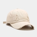 Close-up of distressed beige cotton baseball cap featuring vintage frayed holes and worn brim - Beige