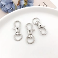 Détail de trois fermoirs mousquetons pivotants argentés pour sacs sur une assiette décorative - 32mm / K Blanc/Argent