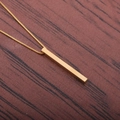 Collana con ciondolo a barra in oro lucido su catena sottile con sfondo in legno scuro - Catena di Rame / Oro