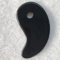 Glossy black heart-shaped resin scraping tool for massage on a white towel - Black Ba Gua Tai Chi Shape