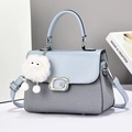 Close-up of light blue leather and woven fabric crossbody bag with silver G buckle and fur ball - Light Blue