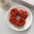 Detail of caramel pleated fabric scrunchie with fine twill texture on white ceramic plate - Orange