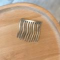 Detail van een zilveren haarkam met 10 gegolfde tanden op een houten dienblad - Metalen legering / Zilver