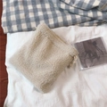 Close-up of cream-colored plush drawstring pouch with soft lamb wool texture on plaid rug - Beige