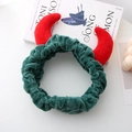 Détail d'un bandeau en peluche verte avec des cornes de diable rouges sur une table - Vert