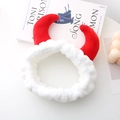 Détail du bandeau en peluche rouge avec cornes de diable posé sur un livre blanc - Blanc