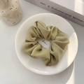 Close-up of a sage green ribbed scrunchie on a white plate with a soft fabric texture - Grass Green
