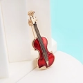 Elegante spilla a violino dorata con smalto rosso e strass su sfondo azzurro - Violino Rosso