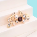 Elegante spilla a nota musicale dorata con strass brillanti, perle bianche e una gemma rossa - Nota d'Oro con Gemma Rossa