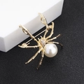 Dettaglio della spilla a ragno dorata con perla bianca e strass scintillanti su nero - Stile Ragno Indurito / Oro + Perla Bianca