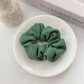 Close-up of deep green twill fabric scrunchie on a white ceramic plate with artistic decor - Green