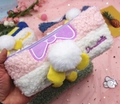 Dettaglio dell'astuccio in peluche in lana d'agnello con fiocco viola e pompon morbido - Rosa Bianco