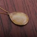 Minimalist gold necklace with a teardrop cream stone pendant on textured wood surface - Yellow Stone Water Drop