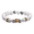 Pulsera de cuentas de turquesa blanca con un dije de calavera dorada en fondo blanco - Dorado