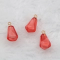 Translucent red pomegranate seed charm with gold loop on white faux fur background - Red