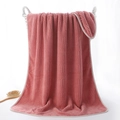 Thick coral pink waffle weave microfibre bath towel draped over a white woven basket - 70x140cm / Lucky Grid/Brick Red