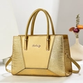 Detailed close-up of golden leather handbag with crocodile pattern texture and metal logo - Gold