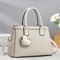 Detail of cream shoulder bag featuring woven texture and a gold heart pendant - Off White