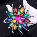 Elegant silver flower brooch with colorful crystals on a dark reflective surface - Colorful