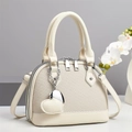 Elegante borsa beige intrecciata con ciondolo a cuore e tracolla su una base bianca - Bianco Sporco