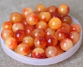 Close-up of orange and white natural agate beads in a transparent bowl on beige fabric - 8mm / Floating Red Pattern