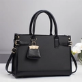 Elegante borsa a mano in pelle nera con trama intrecciata e ciondolo su tavolo bianco - Nero