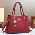 Primer plano de bolso de cuero granate con colgante de perla dorada y logo grabado - Rojo