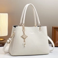 Primer plano de bolso crema con relieve, nudo dorado y detalle de perla - Blanco Roto