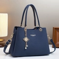 Borsa a tracolla blu navy con finiture dorate e ciondolo di perle su sfondo beige caldo - Blu