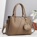 Macro detail of khaki litchi grain leather handbag with V-stitch and mini bag charm - Brown