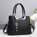 Detail of black embossed leather handbag with silver hardware and clover key charm - Black