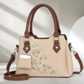 Straw woven tote bag with floral embroidery and brown leather handles in 45-degree view - Light Khaki