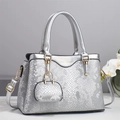 Detail of silver snake-textured handbag featuring a gold logo and a mini charm accessory - Silver