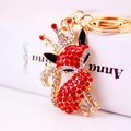 Golden fox keychain with red and white crystals and a crown on a book background - Red