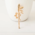 Minimalist golden leaf hair clip with fruit detail on white ceramic background - Four Leaves KC Gold