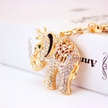 Portachiavi a forma di elefante dorato con strass e corona vicino a un libro bianco - Stile Regolare / Oro