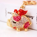 Golden flying pig keychain with sparkling red and white rhinestones on white background - Red
