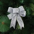 Sparkling silver glitter bow ornament hanging on green Christmas tree branch - Silver