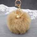 Dettaglio di portachiavi con pompon marrone, chiusura in metallo dorato e decoro con perla - Caffè Medio