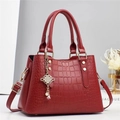 Borsa rossa motivo coccodrillo con manici e ciondolo di perle su un tavolo bianco - Rosso