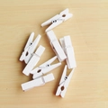 Set of 8 white mini wooden photo clips with metal springs on a light wood surface - White