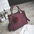 Close-up of wine red matte handbag with plush pom-pom charm in a lifestyle setting - Purple