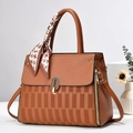 Detail einer braunen Handtasche mit Hahnentritt-Textur und dekorativem Seidenschal-Accessoire - Erdgelb