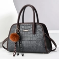 Detail einer grauen Handtasche mit Krokodilprägung, braunen Griffen und Golddekor - Mittel / Grau