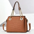 Detail of caramel crocodile pattern handbag with gold chain and top handle on white block - Earthy Yellow