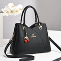 Sac à main trapèze noir élégant avec finitions dorées et charm cerise sur socle blanc - Noir