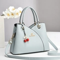 Light blue faux leather handbag with cherry charm and gold hardware on minimalist background - Blue